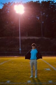 sam standing in a field about us